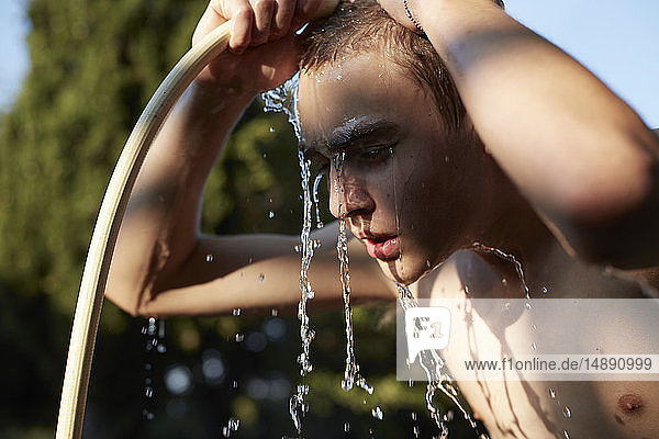 Teenager Junge erfrischt sich mit Wasser aus Gartenschlauch