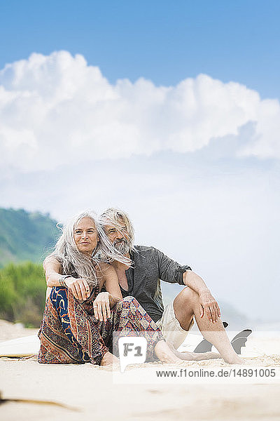 Porträt eines glücklichen älteren Hippie-Paares  das Seite an Seite am Strand sitzt