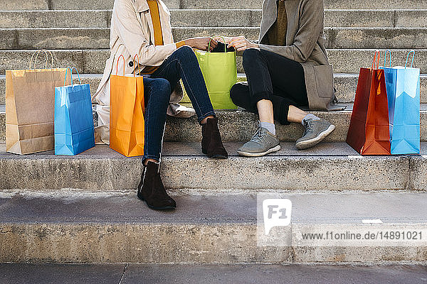 Two women with shopping bags sitting on stairs checking the purchase
