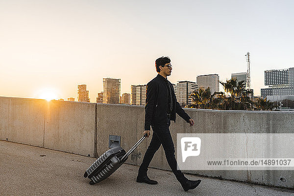 Spanien  Barcelona  junger Geschäftsmann mit rollendem Koffer bei Sonnenuntergang
