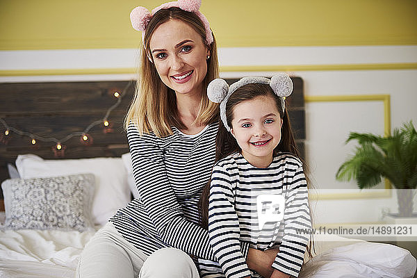 Mother and daighter sitting on bed  wearing plush ears
