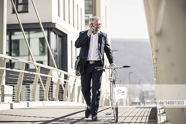 Smiling mature businessman with bicycle talking on cell phone in the city