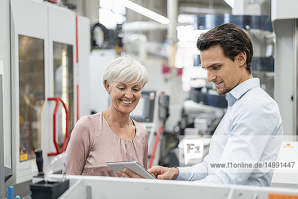 Lächelnder Geschäftsmann und ältere Frau mit Tablettengespräch in einer Fabrik