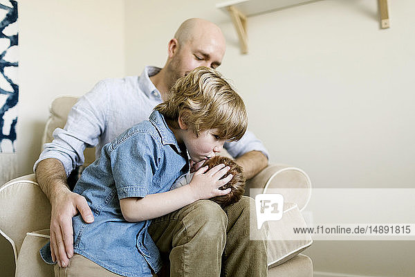 Junge küsst seinen kleinen Bruder auf dem Schoß seines Vaters