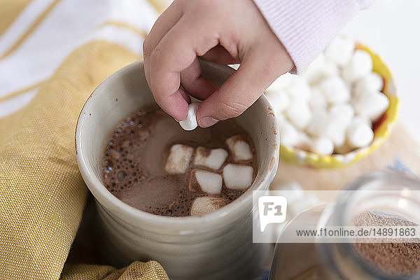 Mädchenhand  die Marshmallows in heiße Schokolade tut