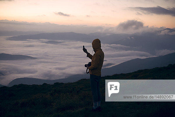 Junger Mann beim Fotografieren mit Smartphone bei Sonnenuntergang in den Karpaten