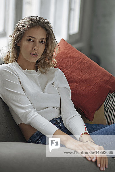 Junge Frau mit weißem Pullover auf dem Sofa