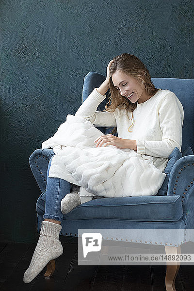 Lächelnde Frau  die in einem Sessel mit weißer Decke sitzt