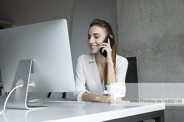 Lächelnde Geschäftsfrau  die ein Telefongespräch am Schreibtisch entgegennimmt