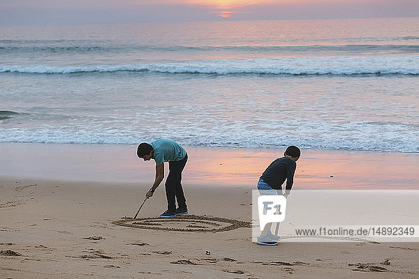 Brothers drawing in sand at sunset
