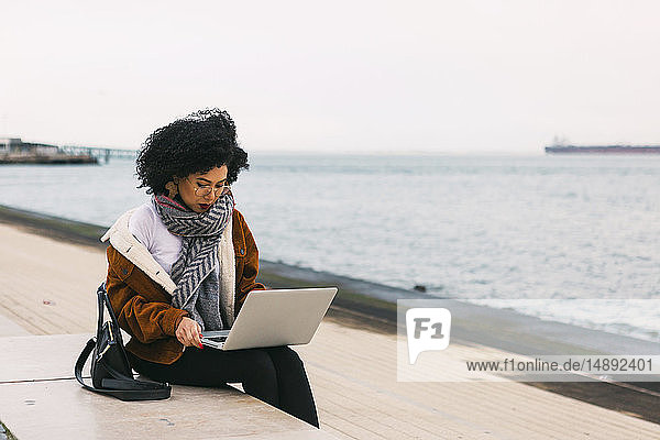Young woman using laptop on waterfront in Lisbon  Portugal