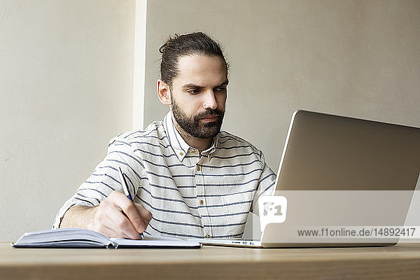 Junger Geschäftsmann mit Laptop schreibt in Notizblock