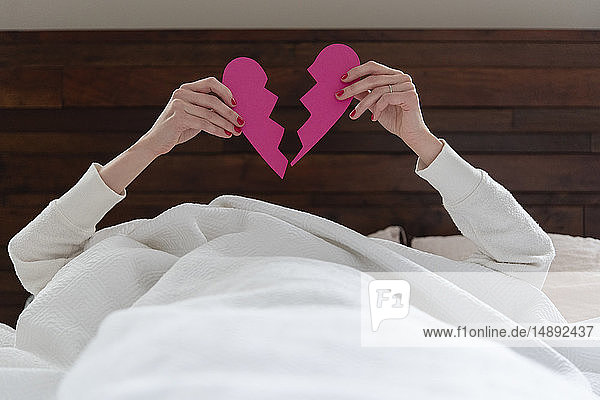 Woman holding aloft pink broken heart while lying in bed