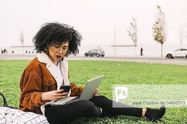 Junge Frau benutzt Laptop und Smartphone im Park