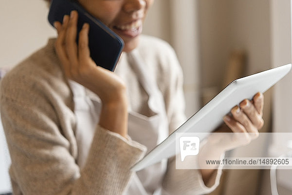Junge Frau  die ein digitales Tablet benutzt  während sie telefoniert