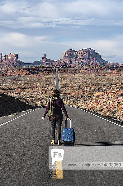 Woman walking with suitcase on road through Monument Valley  Utah  USA