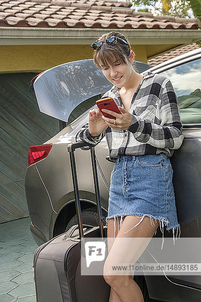 Frau mit Smartphone und Koffer im Auto
