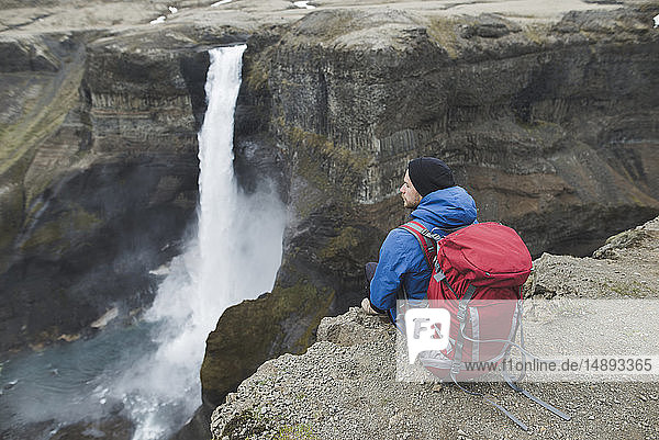 Hiker with backpack on cliff by Haifoss waterfall in Iceland