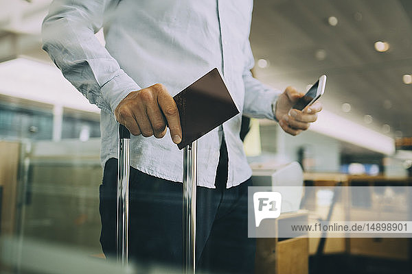 Midsection of businessman holding passport and smart phone at airport