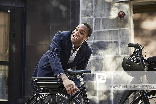 Smiling young male commuter locking electric bicycle while looking away against building in city