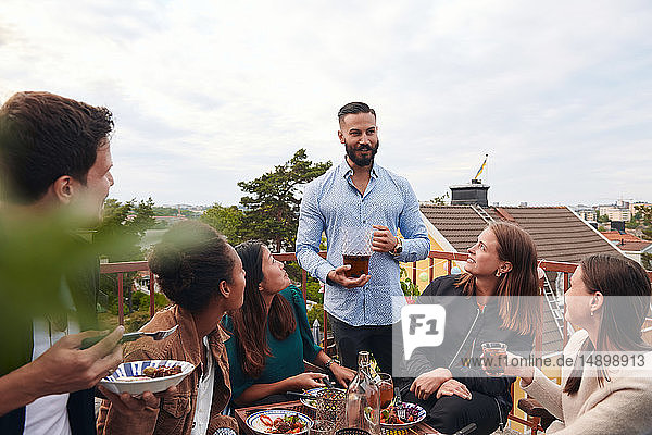 Man talking with friends while holding drink on terrace