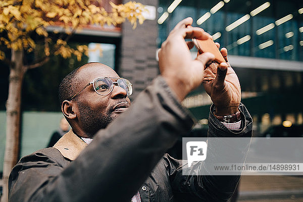 Geschäftsmann fotografiert mit einem Smartphone  während er vor einem modernen Gebäude in der Stadt steht
