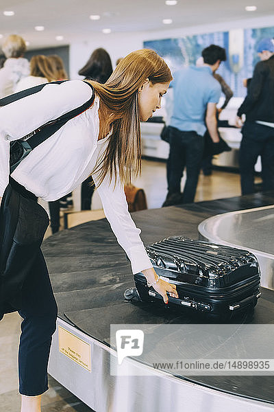 Junge Geschäftsfrau holt Gepäck vom Fließband am Flughafen ab