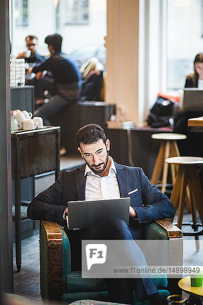 Selbstbewusster Geschäftsmann mit Laptop auf Stuhl sitzend im Kreativbüro