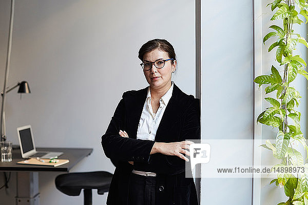 Porträt einer selbstbewussten reifen Geschäftsfrau  die im Büro an der Wand lehnt