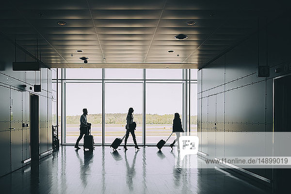Seitenansicht der Silhouette von Geschäftskollegen  die beim Gehen im Korridor am Flughafen Gepäck ziehen