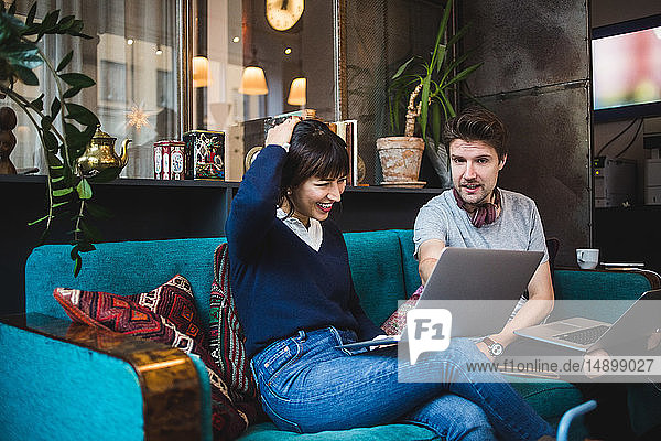 Lächelnde Fachfrau sitzt neben männlichem Kollegen am Laptop im Büro