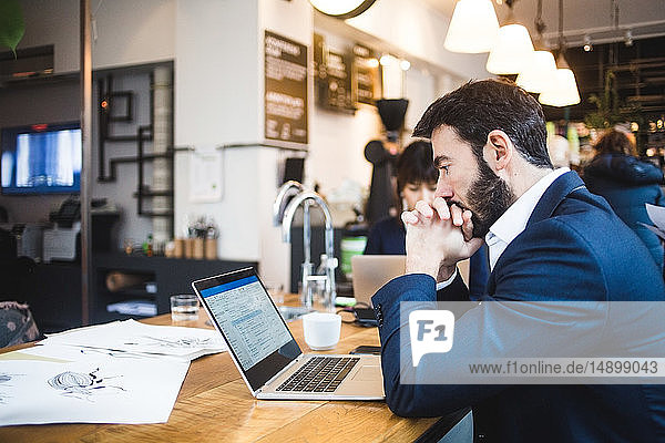 Seitenansicht eines selbstbewussten männlichen Profis  der im Büro auf den Laptop auf dem Tisch schaut