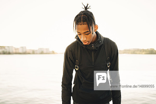 Teenage boy looking down while standing against river
