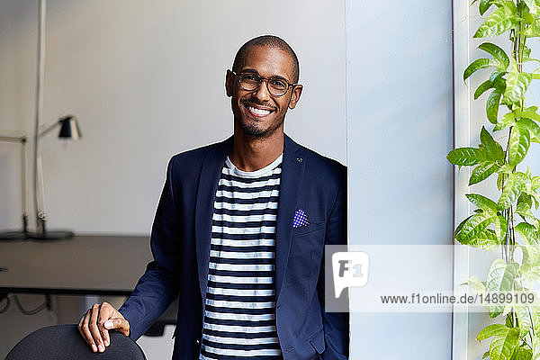 Portrait of smiling male entrepreneur standing by wall in creative office