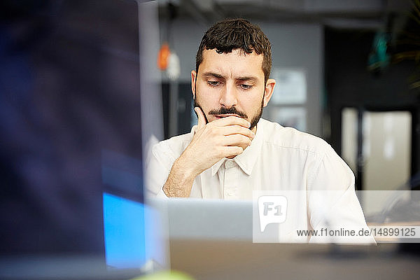 Stressed creative businessman looking at laptop while sitting in office