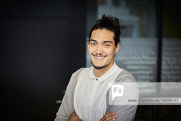 Portrait of smiling young businessman standing with arms crossed in creative office