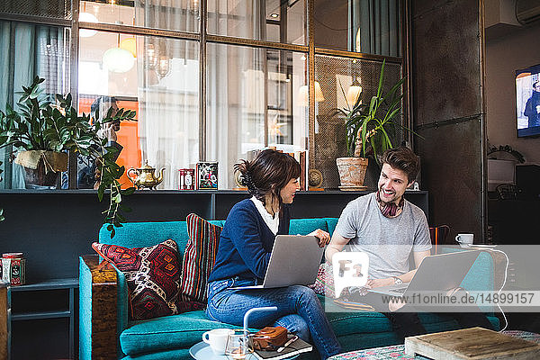 Smiling multi-ethnic female and male professionals discussing over laptop on sofa at office