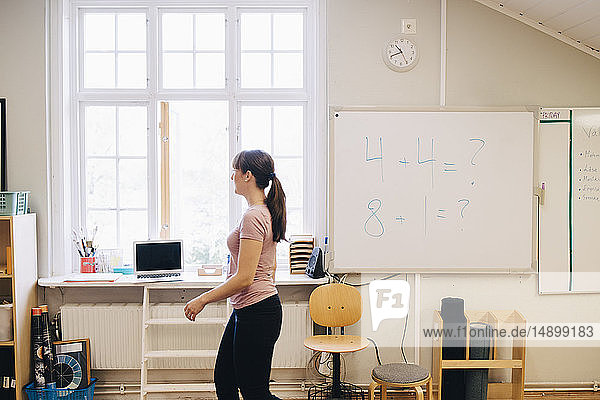 Seitenansicht eines Lehrers  der an einem Whiteboard mit Mathematik im Klassenzimmer vorbeigeht