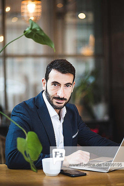Portrait of confident male entrepreneur using laptop while sitting at table in office
