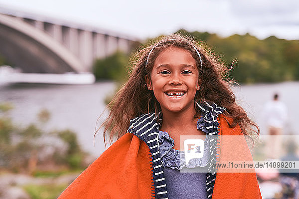 Portrait of cheerful girl with orange blanket standing in park during picnic