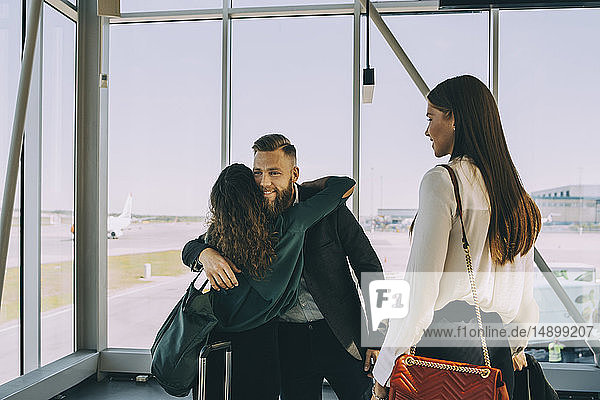 Lächelnde junge Geschäftsfrau  die im Flughafenkorridor stehend Kollegen bei der Begrüßung ansieht