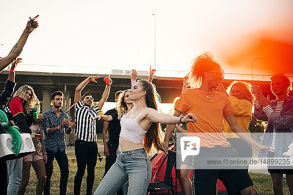 Happy men and women looking at friends dancing in musical event against sky