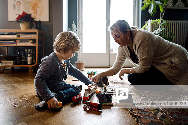Mutter und Tochter spielen mit der Spielzeugeisenbahn  während sie im Wohnzimmer auf dem Hartholzboden sitzen