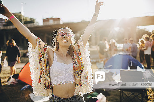 Happy young woman with arms raised enjoying at music event during summer