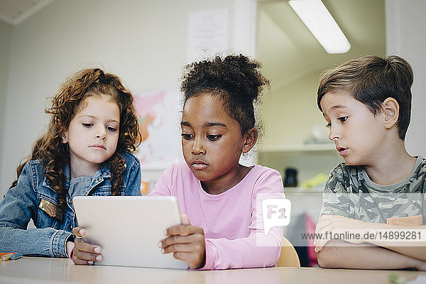 Schulfreunde lernen durch digitales Tablet am Schreibtisch im Klassenzimmer