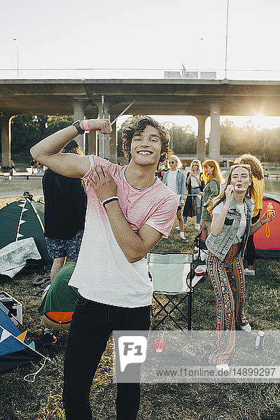 Porträt eines lächelnden Mannes  der seine Muskeln spielen lässt  während er mit Freunden beim Musikfestival genießt