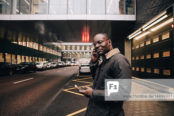 Portrait of businessman with smart phone listening music while standing on road against building in city