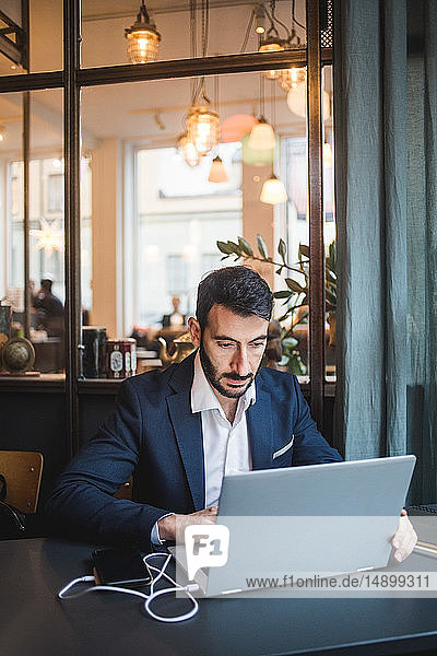 Selbstbewusster Geschäftsmann mit Laptop am Schreibtisch im Kreativbüro