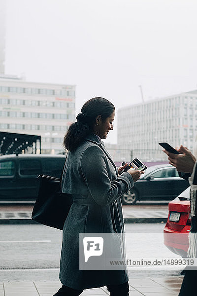 Geschäftsfrauen benutzen Mobiltelefone beim Gehen auf dem Bürgersteig gegen den Himmel in der Stadt
