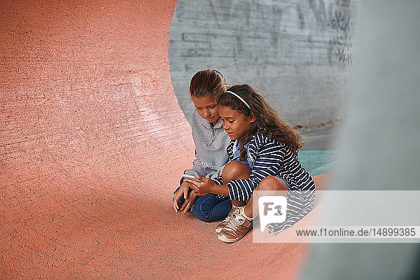 Schwestern benutzen Mobiltelefon  während sie im Tunnel auf dem Spielplatz sitzen